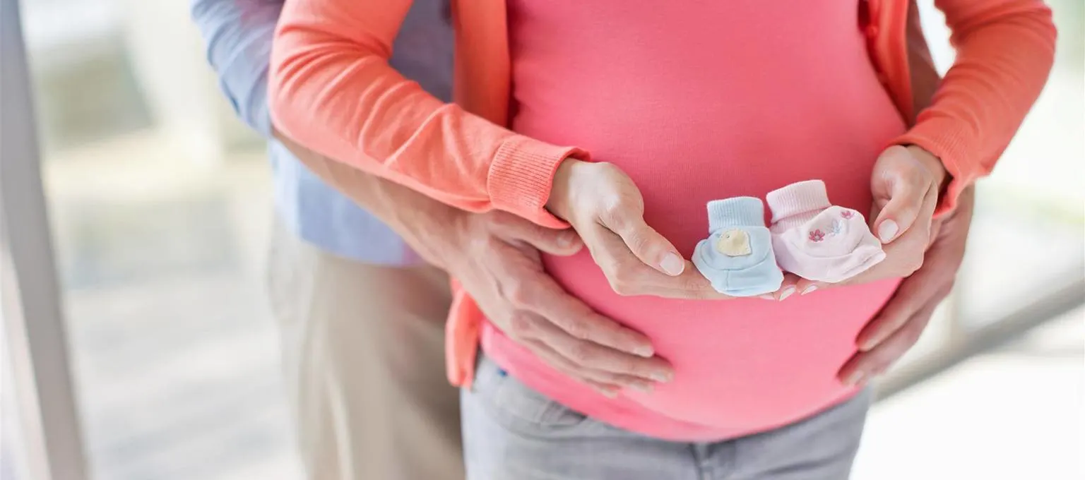 Pregnant woman holding shoes for twins