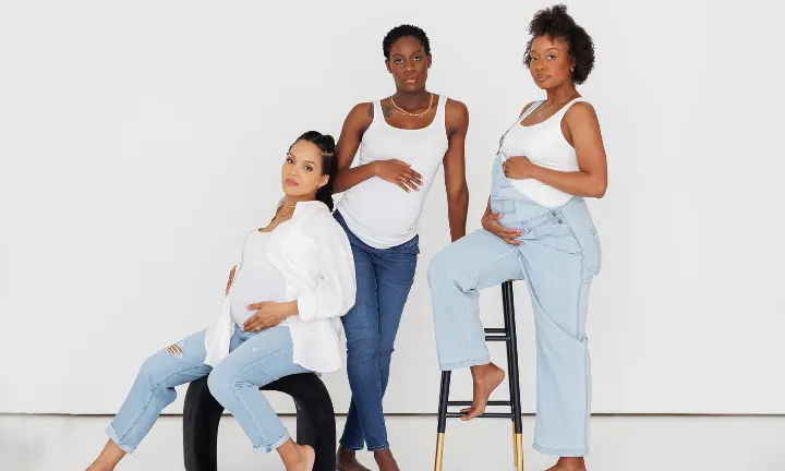 Three pregnant women posing with hands on bellies and looking confidently into the camera